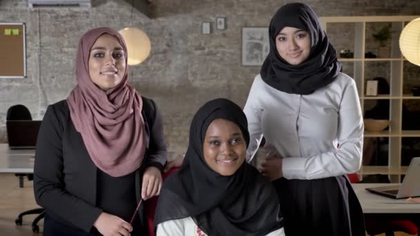 Equipo de negocios de tres jóvenes musulmanas en hijab mirando a cámara y sonriendo en la oficina moderna — Vídeos de Stock