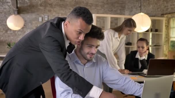 Два молодых бизнесмена наблюдают за ноутбуком в офисе, общаются с технологиями, обсуждают фон, рабочую концепцию, бизнес-концепцию, коммуникационную концепцию — стоковое видео