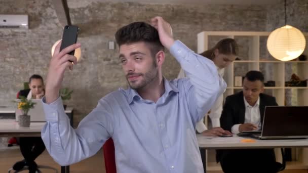 若いビジネスマンがオフィスでスマート フォンで selfie を作っている、技術、作業コンセプト、ビジネス コンセプト、コミュニケーション コンセプトと彼の同僚のネットワー キング — ストック動画
