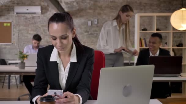 Junge Geschäftsfrau liest und tippt Nachricht auf Smartphone im Büro, lächelt, ihre Kollegen vernetzen sich mit Technologien, Arbeitskonzept, Geschäftskonzept, Kommunikationskonzept, Dolly — Stockvideo