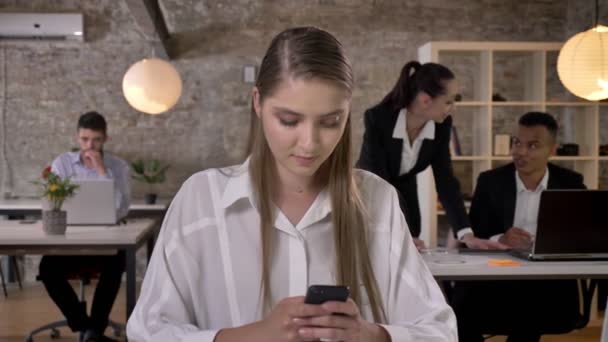 Junge schöne Geschäftsfrau tippt im Büro auf dem Smartphone, ihre Kollegen vernetzen sich mit Technologien, Arbeitskonzept, Geschäftskonzept, Kommunikationskonzept — Stockvideo
