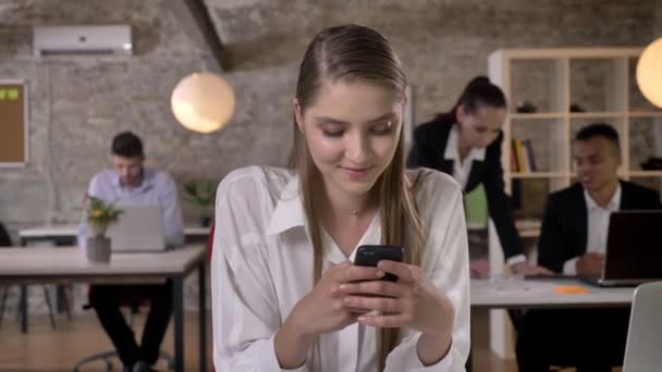 Jeune femme d'affaires douce tape sur smartphone au bureau, ses collègues sont en réseau avec les technologies, concept de travail, concept d'entreprise, concept de communication — Video