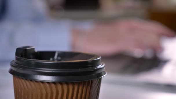 Xícara de café na mesa no escritório, mãos de homem de negócios estão digitando no laptop no fundo, fundo turvo, conceito de trabalho — Vídeo de Stock