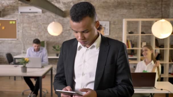 Junger afroamerikanischer Geschäftsmann tippt im Büro auf Tablet, seine Kollegen vernetzen sich mit Technologien, Arbeitskonzept, Geschäftskonzept, Kommunikationskonzept — Stockvideo