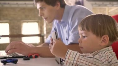 Küçük çocuk oynarken üzerinde tablet ne zaman genç babası laptop modern ofisinde otururken, çalışma