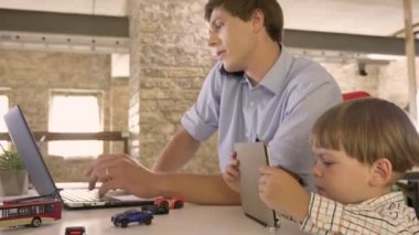 Genç Baba dizüstü bilgisayarda çalışan ve, küçük oğlu tablet, meşgul ve konsantre izlerken Evet