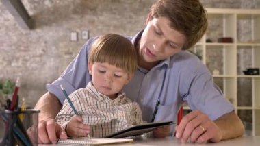 Tablet vasıl, modern ofis arka planı arıyorum Genç babası masada oturan ve kağıt üzerinde yazılı küçük çocuk