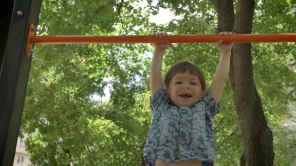 Jovem pai ajudando seu filho a fazer pull-ups, pai treinando filho no parque, sorrindo — Vídeo de Stock