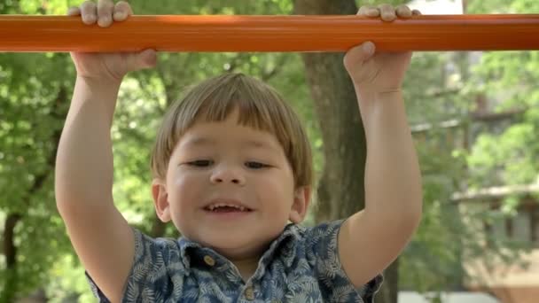 Klein kind doen pull-up en zijn jonge vader helpen hem, opleiding in park, zomer — Stockvideo