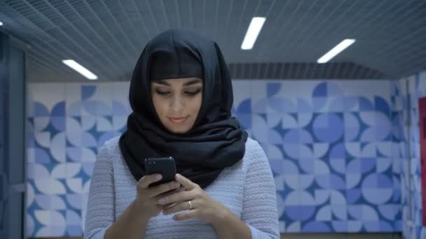 Young charming muslim woman in hijab is typing message on smartphone in underpass, watching at camera, religion concept, communication concept — Stock Video