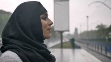 Hijab genç Müslüman kadın Tren Tren İstasyonu, yağmur, din kavramı, kentsel kavramı bekliyor. Hava kavramı, yan görünüm