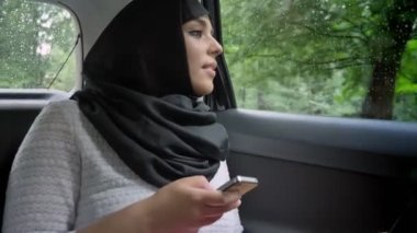 Hijab genç Müslüman kadın tutarak smartphone, taşıma kavramı, iletişim kavramı, hava konsept araba, yağmurlu penceresinde izliyor