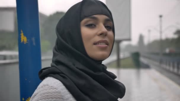 Mujer musulmana joven en hijab está esperando tren en la estación de tren, la lluvia, el concepto de religión, el concepto urbano. concepto meteorológico — Vídeos de Stock