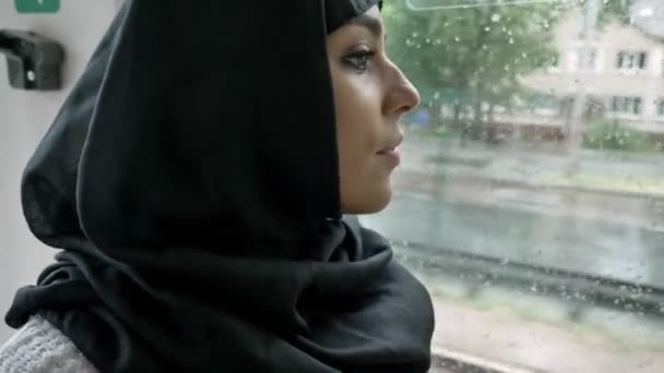 Jovem mulher muçulmana no hijab está assistindo na janela em trólebus, tempo chuvoso . — Vídeo de Stock