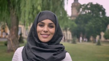 Hijab genç güzel Müslüman kızı ayakta ve gündüz, kötü havada gülümseyerek kameraya, Bina arka plan, religiuos kavramı, arka plan bulanık izliyor