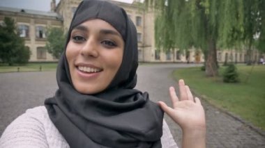 Hijab genç mutlu Müslüman kız video, hey söyleyerek, mavi hava, iletişim kavramı, dini kavramı el sallayarak, arka planda bina yapıyor