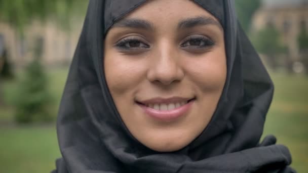 Gezicht van jonge sencere moslim meisje in hijab lacht overdag, bij slecht weer, kijken in de camera, religiuos concept, onscherpe achtergrond — Stockvideo