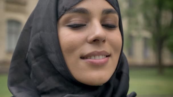 Jeune belle fille musulmane dans le hijab tourne la tête à la caméra et souriant dans la journée, par mauvais temps, concept religiuos, fond flou — Video