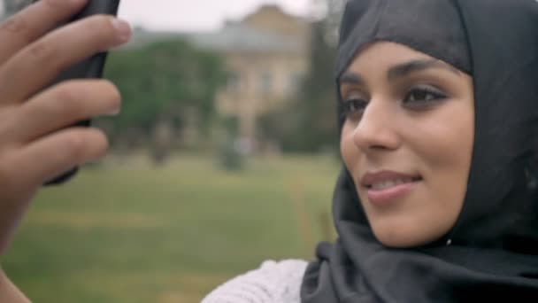 Joven hermosa chica musulmana en hijab está haciendo selfie en el teléfono inteligente en el clima azul, concepto de comunicación, concepto religioso, fondo borroso — Vídeos de Stock