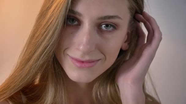 Jonge blonde vrouwen met blauwe ogen in de camera kijken en het aanraken van haar haren, glimlachend — Stockvideo