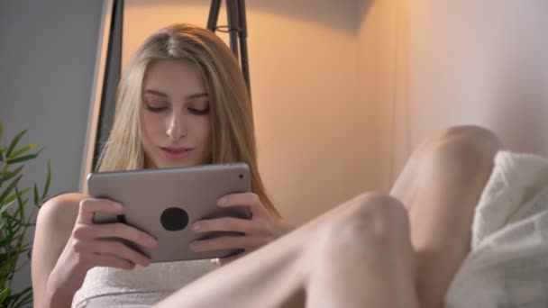 Giovani donne bionde in lingerie sdraiate sul divano e usando tablet, sorridenti, felici — Video Stock