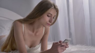 Genç seksi model üzerinde kötü yalan ve telefon, beyaz modern yatak odası arka plan üzerine yazarak iç çamaşırı