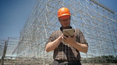 Tablet kullanma ve çatık, zemin, ciddi ve endişe üzerine metal konstrüksiyon kask içinde genç mimar