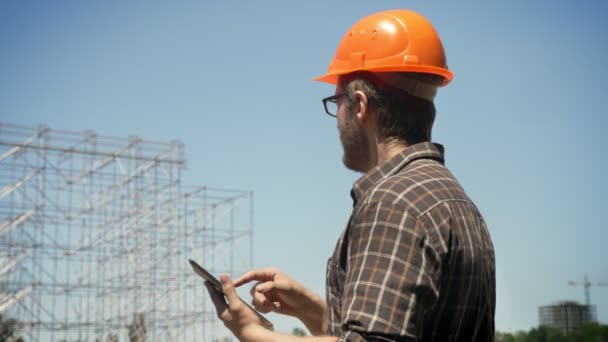 Joven arquitecto en gafas diseñando su nuevo proyecto, mirando la instalación de metal y comprobando el plan en la tableta, confiado — Vídeos de Stock