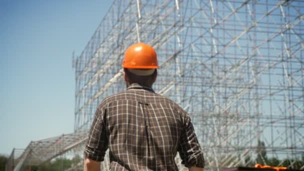 Espalda del arquitecto masculino en casco caminando hacia la instalación de metal en el fondo — Vídeos de Stock