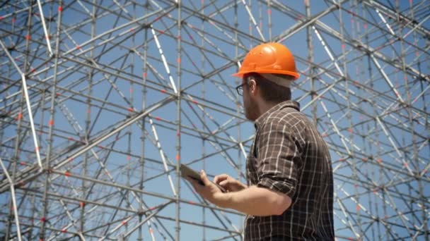 Joven arquitecto confiado diseñando su nuevo proyecto, sosteniendo la tableta y mirando la instalación de metal — Vídeos de Stock