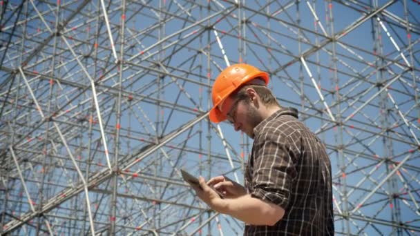 Junger Architekt hält Tablet in der Hand und betrachtet Metallinstallation im Hintergrund, plant und entwirft neues Projekt — Stockvideo