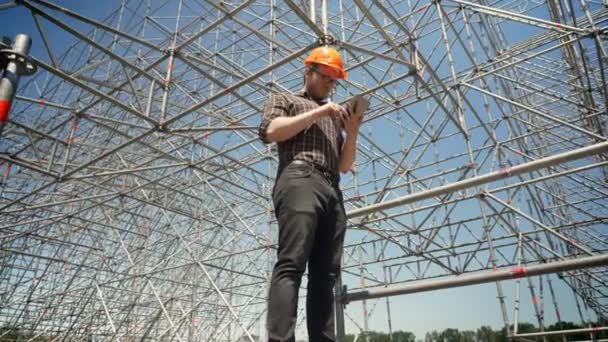 Junge Architektin steht mit Tablet und betrachtet Metallinstallation im Hintergrund, plant und entwirft neues Projekt — Stockvideo