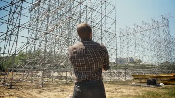 Tyłu młody człowiek stojący na polu słomy i patrząc na konstrukcji metalowej — Wideo stockowe