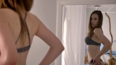 Genç seksi kız iç çamaşırı duran ve vücut ayna ve kendisi dönüm dokunaklı bakarak