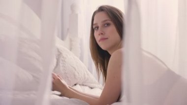 Genç seksi kız iç çamaşırı yatakta yatıyor ve kameraya izlerken, saç, dokunaklı dudak, ilk satırdaki tül ile oynarken, kavram flört