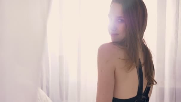 La silhouette della giovane ragazza sexy in lingerie è seduta sul letto e guarda la fotocamera, tulle sulla finestra, luce del sole, concetto di relax, concetto di flirt — Video Stock