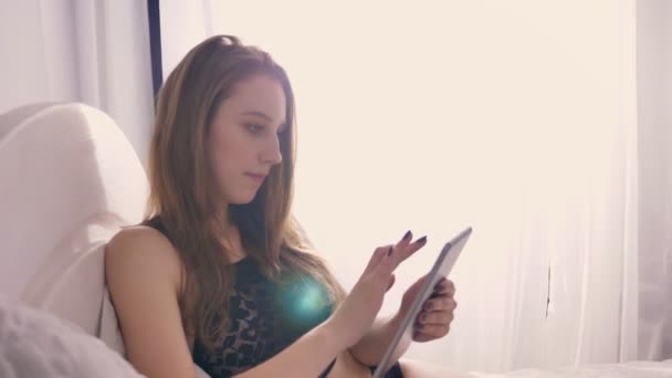 Jonge sexy meisje in lingerie is op bed te leggen en kijken naar tablet, zonlicht, ontspannen concept, flirt concept, communicatieconcept — Stockvideo