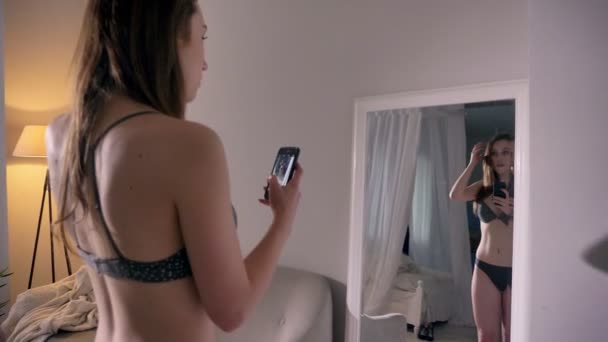 Jeune fille sexy est debout dans la lingerie et de prendre des photos, regarder dans le miroir, concept de communication — Video