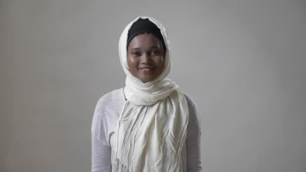 年轻的非洲穆斯林女孩在面纱站立和微笑, 观看在照相机, religioun 概念, 灰色背景 — 图库视频影像