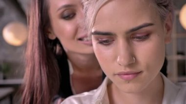 Bir kulakta ofiste başka bir kadının çalışma sırasında gülümseyen ve çekici fısıldayan genç güzel lezbiyen