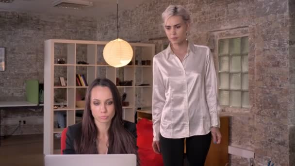 Две молодые лесбиянки в офисе, очаровательная женщина трогает другую блондинку, сидит на столе — стоковое видео