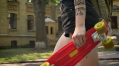 Olağanüstü genç kadın Üniversitesi uzak yürüme ve kaykay tutan dövmeli el ile