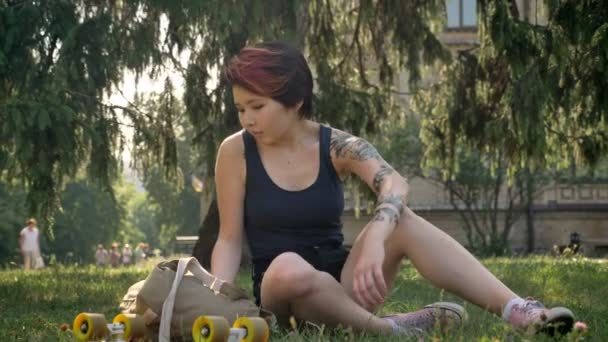 Ασιατικές νεαρές γυναίκες με τατουάζ μόνιμη από γρασίδι και πηγαίνουν στο Πανεπιστήμιο, κρατώντας σακίδιο και skateboard — Αρχείο Βίντεο