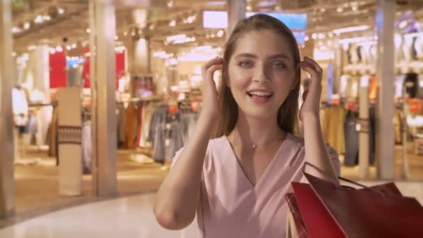 Joven chica atractiva va de compras en el centro comercial, relojes en bolsas, expresar sorpresa, sonrisa, concepto de compras, concepto de moda — Vídeos de Stock