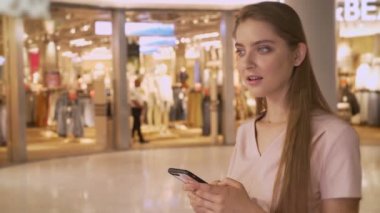 Genç çekici kız kameraya, alışveriş kavramı, moda kavramı, iletişim kavramı izlerken Mall, Smartphone, chattiong alışveriş gidiyor