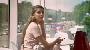 Genç güzel kız büyük pencereler kafede oturup gündüz, holding smartphone, kentsel kavramı