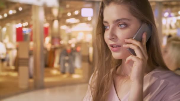 Joven chica atractiva va de compras en el centro comercial, hablando por teléfono, concepto de compras, concepto de moda, concepto de comunicación — Vídeo de stock