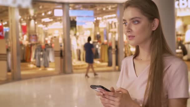 Ung vacker flicka går shopping i gallerian, chattiong på smartphone, shopping koncept, fashion-konceptet, kommunikationskoncept — Stockvideo