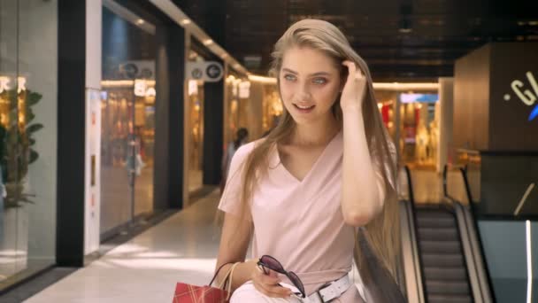 Fiatal vonzó lány állandó Mall, könyv táskák, nézi a kamerát, megható haj, vásárlás koncepció, divat fogalma — Stock videók