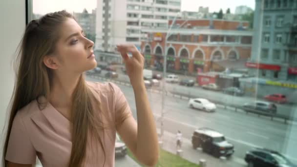 Joven hermosa chica está sentado en la ventana, tocando el pelo, mirando a la cámara, concepto de ensueño — Vídeos de Stock